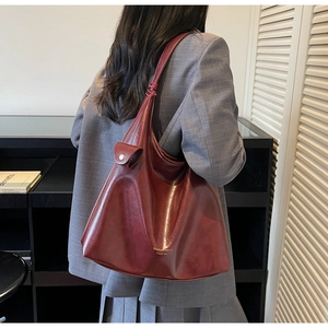 Détail du sac cabas en cuir bordeaux avec bandoulière nouée et bouton pression doré