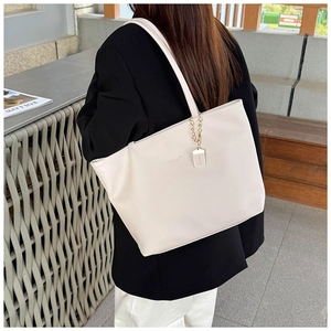 Close-up of cream lychee leather tote bag with gold chain charm on a shoulder