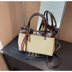 Detail of a retro tote bag with beige fabric, dark brown faux leather, and a metal key charm