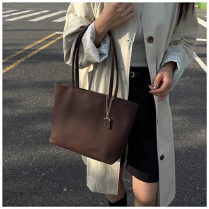 Detailed close-up of brown pebbled leather tote bag with elegant gold chain ornament