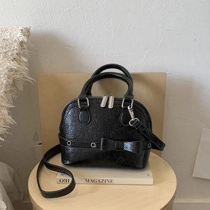 Glossy black bowling bag with bow and metal eyelets on a wooden stool scene