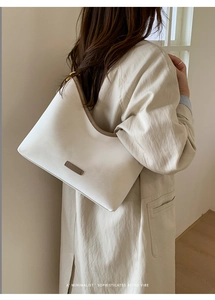 Detail of minimalist white hobo bucket bag with brown trim on a model in trench coat