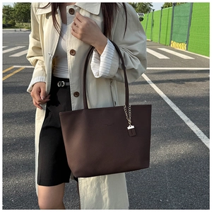 Close-up of dark brown lychee leather tote bag with gold chain pendant detail