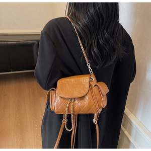 Détail d'un sac en cuir matelassé marron avec chaîne dorée sur un blazer noir