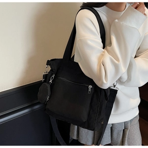Black canvas tote bag with zipper pocket and round coin purse shown on model shoulder