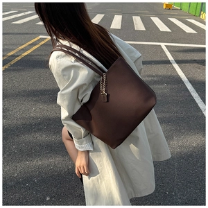 Detail view of dark brown tote bag with leather grain texture and golden chain on a model