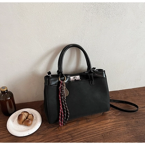 Detail of black suede matte handbag with woven pendant and silver twist lock on wood