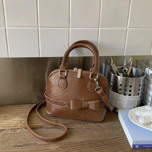 Macro view of brown leather-texture shell bag with bow detail and silver zipper