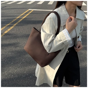 Brown leather tote bag with lychee texture carried by a model in a beige trench coat
