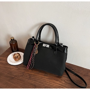 Detail of black faux leather handbag with silver twist lock and woven tassel charm