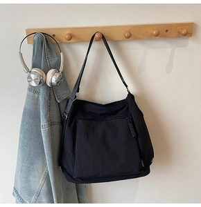 Detail of black nylon tote bag with SHUNUO label hanging on wooden rack with accessories