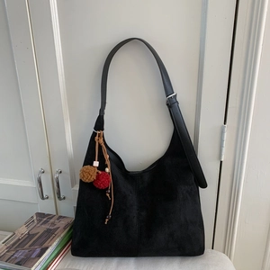 Détail du sac hobo noir mat avec bandoulière réglable et breloque pompon décorative