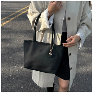 Detail of black pebbled leather tote bag with gold chain charm on urban street