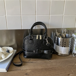 Close-up of black shell bag featuring leather bow detail and silver metal grommets