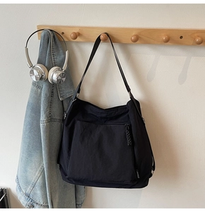 Detail of black nylon tote bag showing front zipper pocket and woven puller on wooden hook