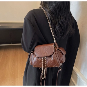 Détail d'un sac bandoulière marron foncé matelassé avec chaîne et petites poches latérales