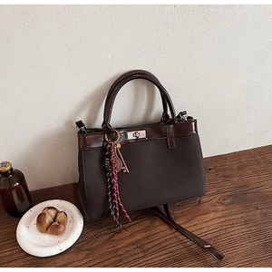 Detail of vintage coffee brown tote bag with metal buckle and knot charm on wood table