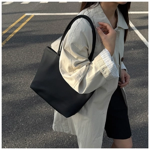 Detail view of black pebble grain tote bag styled with an elegant beige trench coat