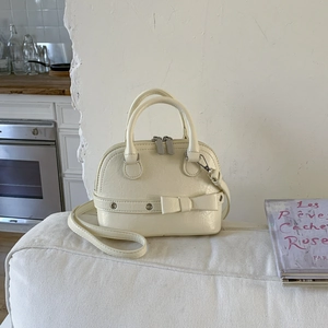 Close-up of creamy white shell bag with bow detail and textured leather surface