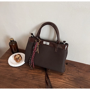 Detail of dark brown suede handbag featuring silver twist lock and woven key charm
