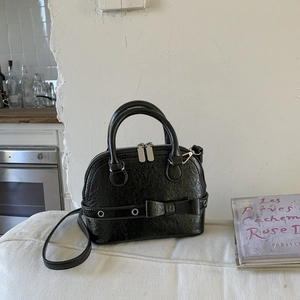 Detail of black shell bag with vintage crackle texture and metal eyelet bow decoration