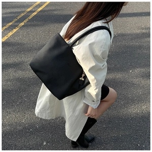 Close-up of black lychee leather tote bag with metal chain on a trench coat model