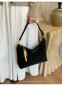 Detail of matte black hobo bag with gold hardware and creative wooden bead charm
