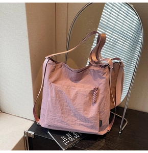 Detail of dusty pink nylon tote bag showing front zip pocket and brand label