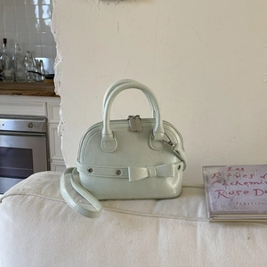 Detail of mint green shell bag featuring polished leather and decorative bow on white sofa