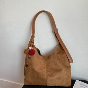 Détail d'un sac hobo en daim marron mat avec bandoulière réglable et breloque à pompons