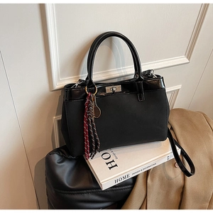 Detail of black matte tote bag featuring silver twist-lock and woven tassel accessory