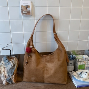 Gros plan du sac hobo en daim marron avec bandoulière réglable et pompon décoratif