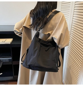Detail of a large black canvas tote bag showing the side logo tag on a female model