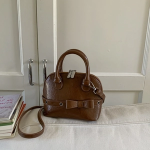 Close-up of vintage brown shell bag with shiny leather texture and decorative bow detail