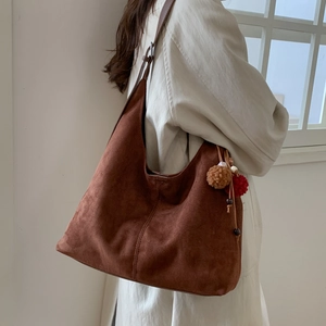 Détail d'un grand sac cabas en daim marron avec pompon en peluche et perles en bois