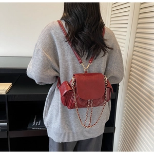 Détail d'un mini sac à dos matelassé bordeaux avec chaînes dorées sur un pull gris