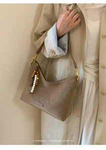 Detail of taupe retro bucket bag with decorative wooden beads on a stylish trench coat