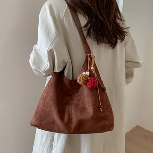Détail du sac hobo en daim marron avec des breloques boules en peluche et perles en bois