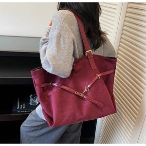 Detailed close-up of large burgundy suede tote bag with metallic buckles and rivets