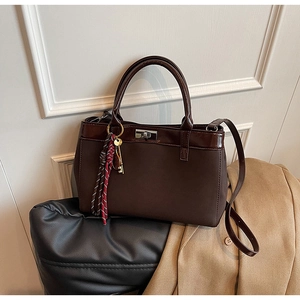 Detail of dark brown leather handbag with silver twist lock and striped tassel accent