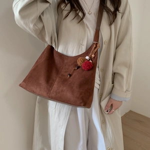 Détail du sac bandoulière en daim marron foncé avec pompons en fourrure rouge et marron