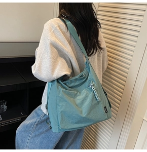 Detail view of cyan nylon tote bag with wide strap and side zip on person
