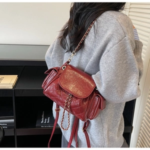 Détail du sac à dos matelassé rouge foncé avec bandoulière chaîne porté de profil