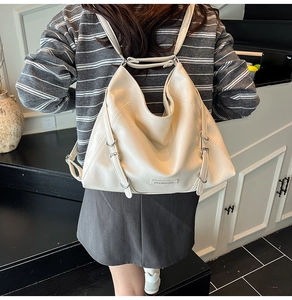 Detail of a large ivory leather tote bag with metal brand tag and adjustable shoulder strap