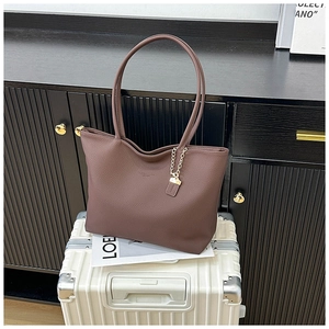 Detail of dark brown lychee grain leather tote bag with gold chain charm on a white suitcase