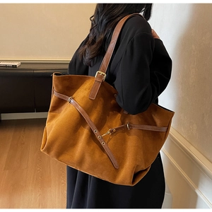 Detail view of large brown suede tote bag featuring metallic rings and buckle straps