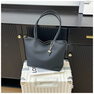 Detail of black lychee grain leather tote bag with gold chain on a white suitcase