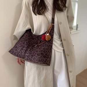 Détail d'un sac cabas léopard avec bandoulière marron et pendentif pompon en peluche