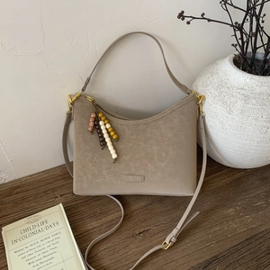 Detail view of taupe saddle bag with wooden bead charm on a vintage wooden desk