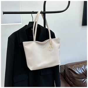 Detail view of cream white tote bag with lychee grain texture and gold chain logo tag